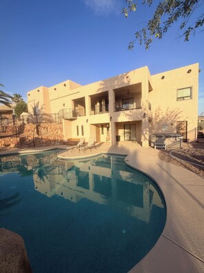 A pool area with a clear blue pool, a stone wall, and a building with balconies. - Large home panoramic lake views, boat parking, pool, game room, ice machine! (Lake Havasu City)