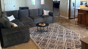 Una sala de estar con un sofá seccional gris, una mesa de centro y un tapete estampado.