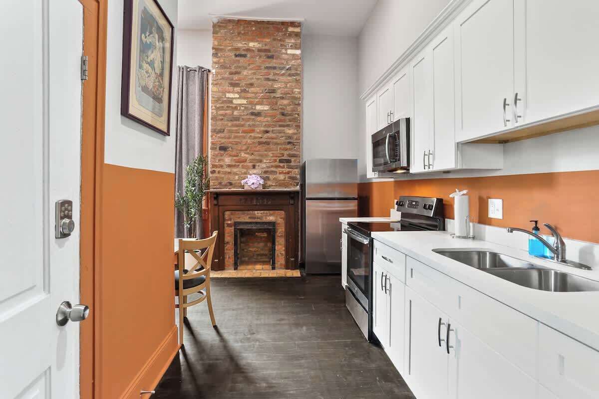 Una cocina con armarios blancos, chimenea de ladrillo, refrigerador de acero inoxidable y microondas.