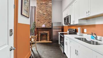 Una cocina con armarios blancos, chimenea de ladrillo, refrigerador de acero inoxidable y microondas.