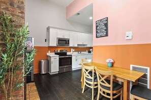 A modern kitchen with white cabinets, a microwave, and a wooden dining table with chairs. - Explore NOLA: Studio 6 Blocks from French Quarter (New Orleans)