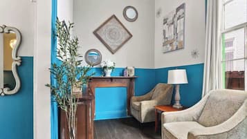 A room with a blue and white color scheme, featuring two armchairs, a small table with a lamp, and decorative wall art.