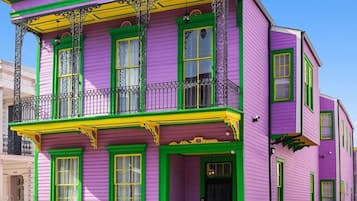Ein zweistöckiges Gebäude mit einer leuchtend violetten Fassade, grünem Zierrat und einem Balkon mit aufwendigen Metallgeländern.