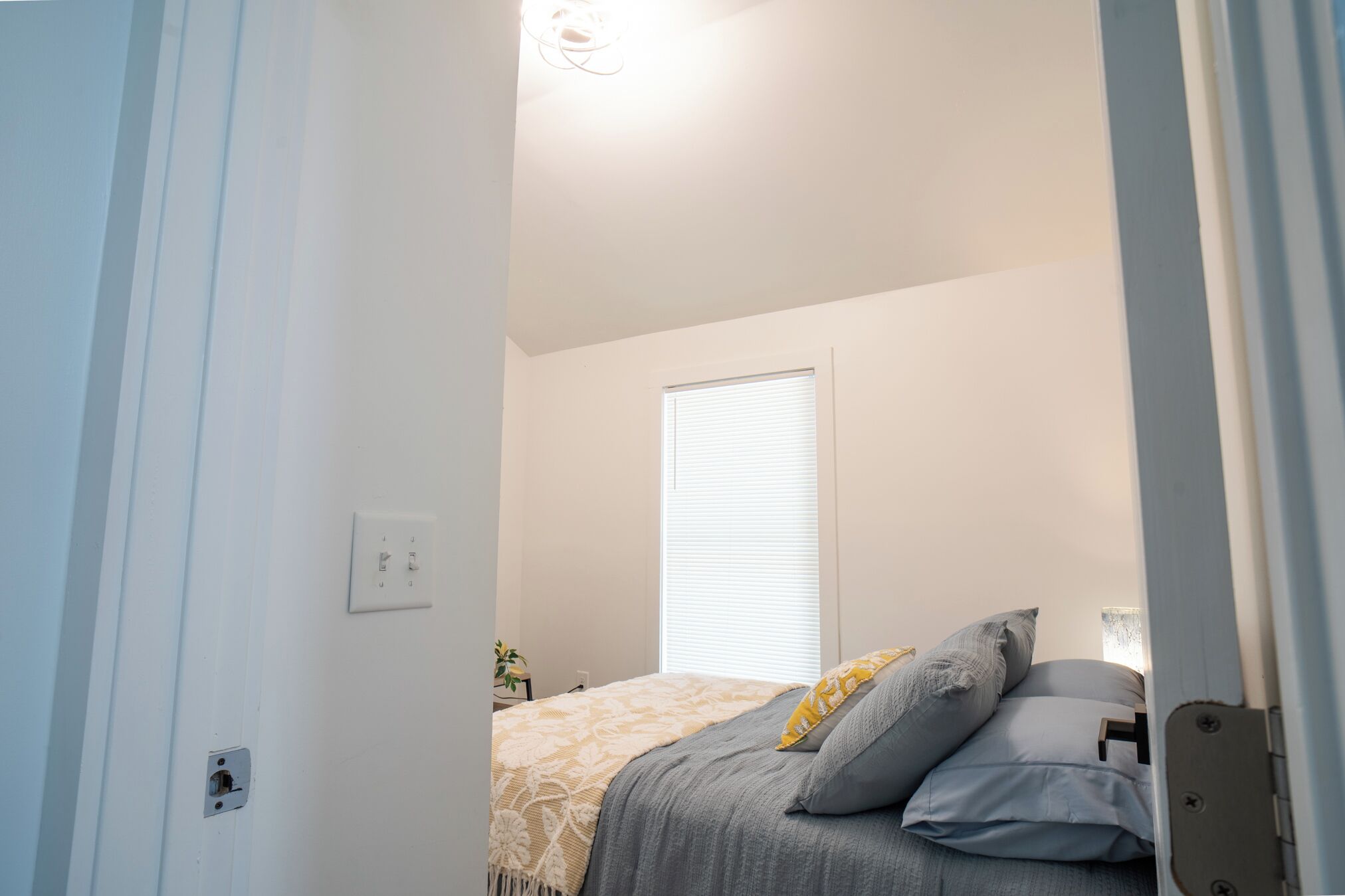 A bedroom with a bed, a window with blinds, and a door.