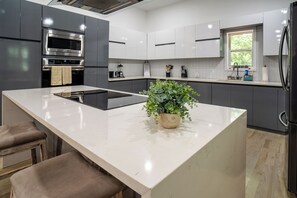 Eine moderne Küche mit einer zentralen Kochinsel, grauen Schränken, Edelstahlgeräten und einem Blumentopf.