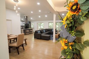 A modern living room with a sectional sofa, a dining area with a wooden table and chairs, and a kitchen in the background. - The White Brick Cottage located in Buckhead Area: Peaceful and Charming (Atlanta)