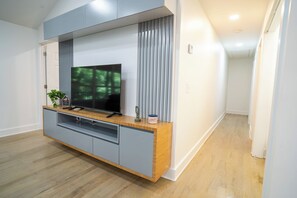 A modern entertainment unit with a flat-screen TV, wooden accents, and a built-in cabinet. - The White Brick Cottage located in Buckhead Area: Peaceful and Charming (Atlanta)