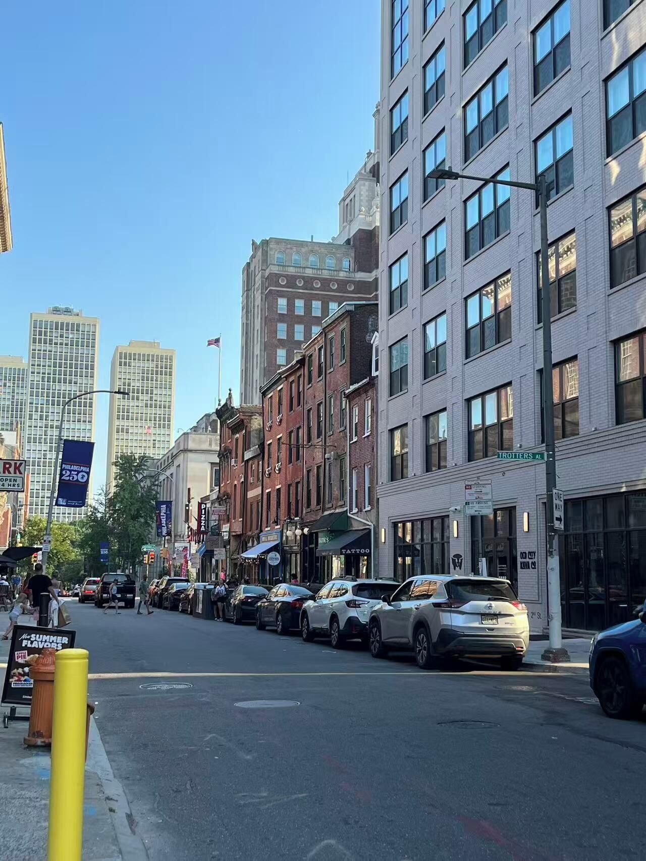 A street view with buildings, parked cars, and a clear sky.