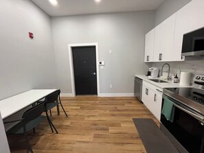 A modern kitchen with white cabinets, a black door, and a dining area with a table and chairs. - Brand New Modern 1BR in Old City Philadelphia (Philadelphia)