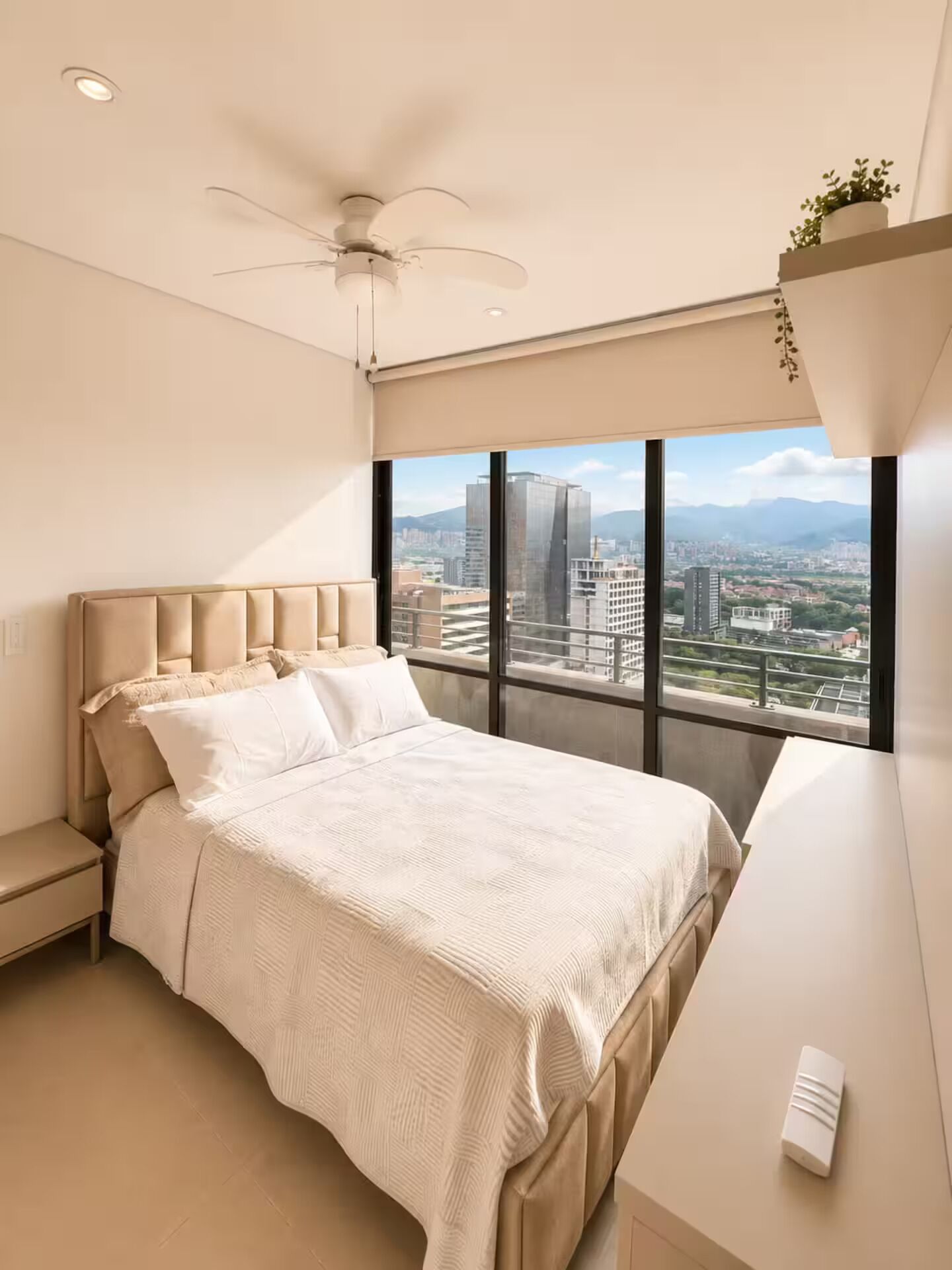 A modern bedroom with a large bed, a ceiling fan, and a city view through the window.