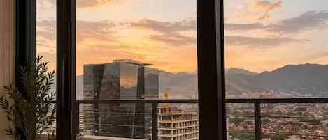 A room with large windows overlooking a cityscape and mountains during sunset.