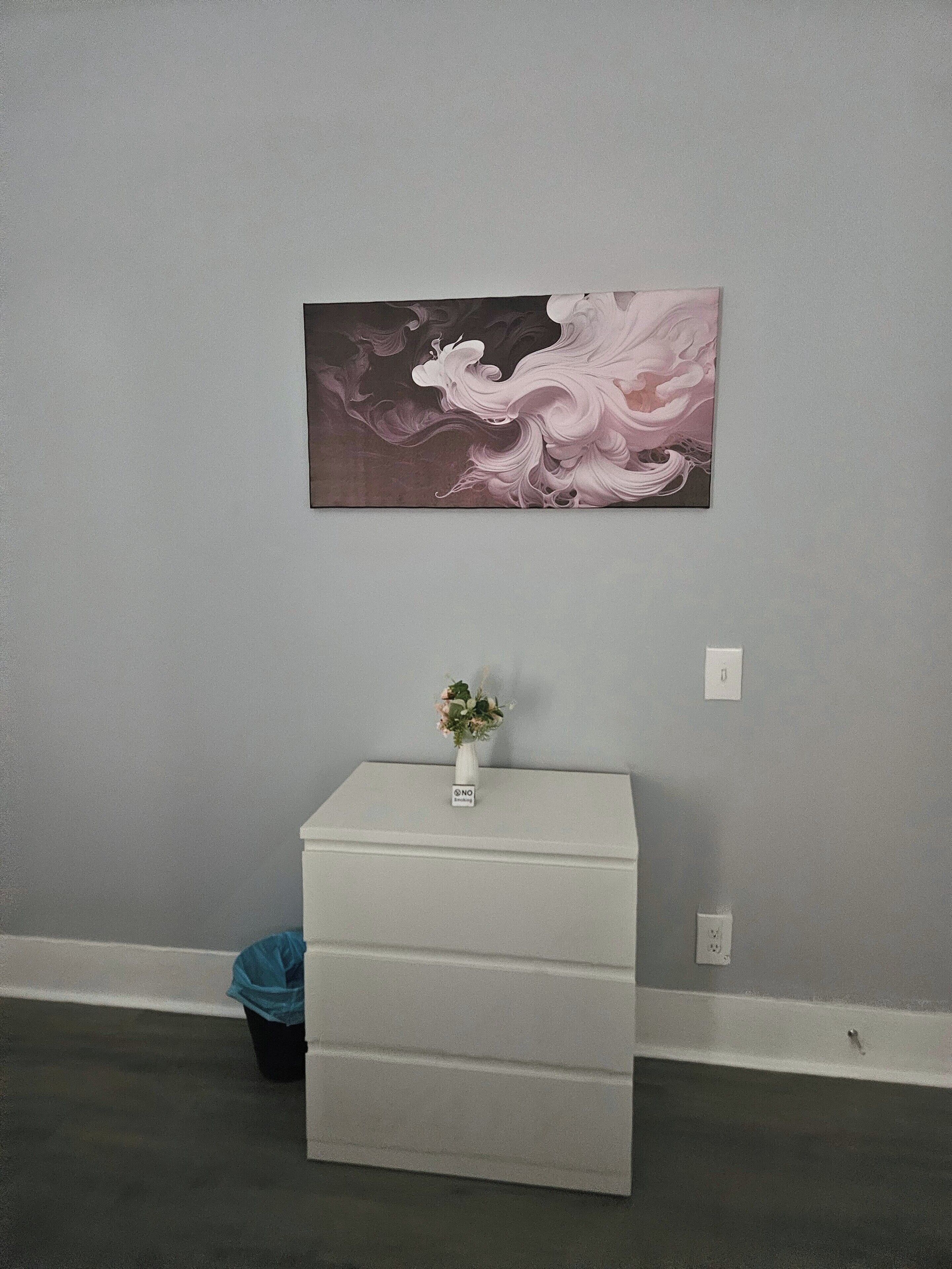 Une pièce avec un mur gris, une armoire blanche ornée d’un vase de fleurs et un tableau.