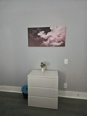 A room with a grey wall, a white cabinet with a vase of flowers, and a painting.