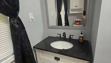 Un baño con tocador blanco, encimera negra y espejo sobre el lavabo.
