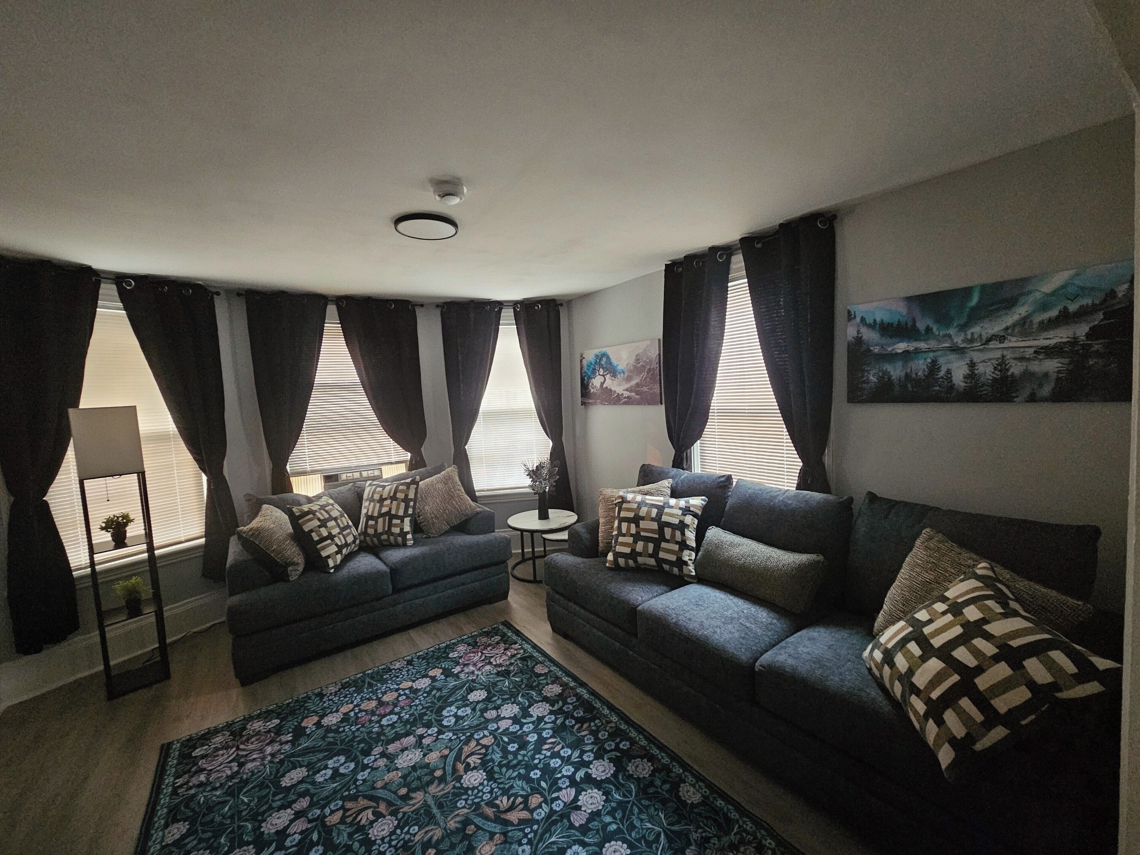 A living room with two sofas, a coffee table, a floor lamp, and a large window with curtains.