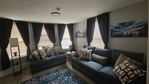 A living room with two sofas, a coffee table, a floor lamp, and a large window with curtains.