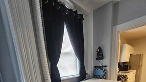 Un espacio para lavandería con lavadora y secadora, una ventana con cortinas, y una zona de cocina visible a través de una puerta abierta.