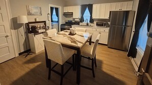 Cocina compacta con mesa, sillas, refrigerador, microondas, estufa y alacenas.