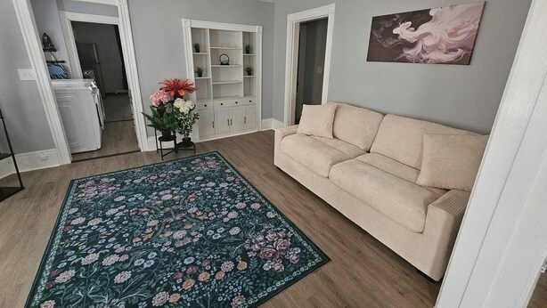 Una sala de estar con un sofá color beige, un tapete floral y un mueble blanco para el entretenimiento.