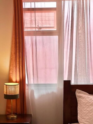 A room with a bed, a bedside table with a lamp, and a window with curtains. - Casa Esmeralda Boutique Hotel (San Jose)
