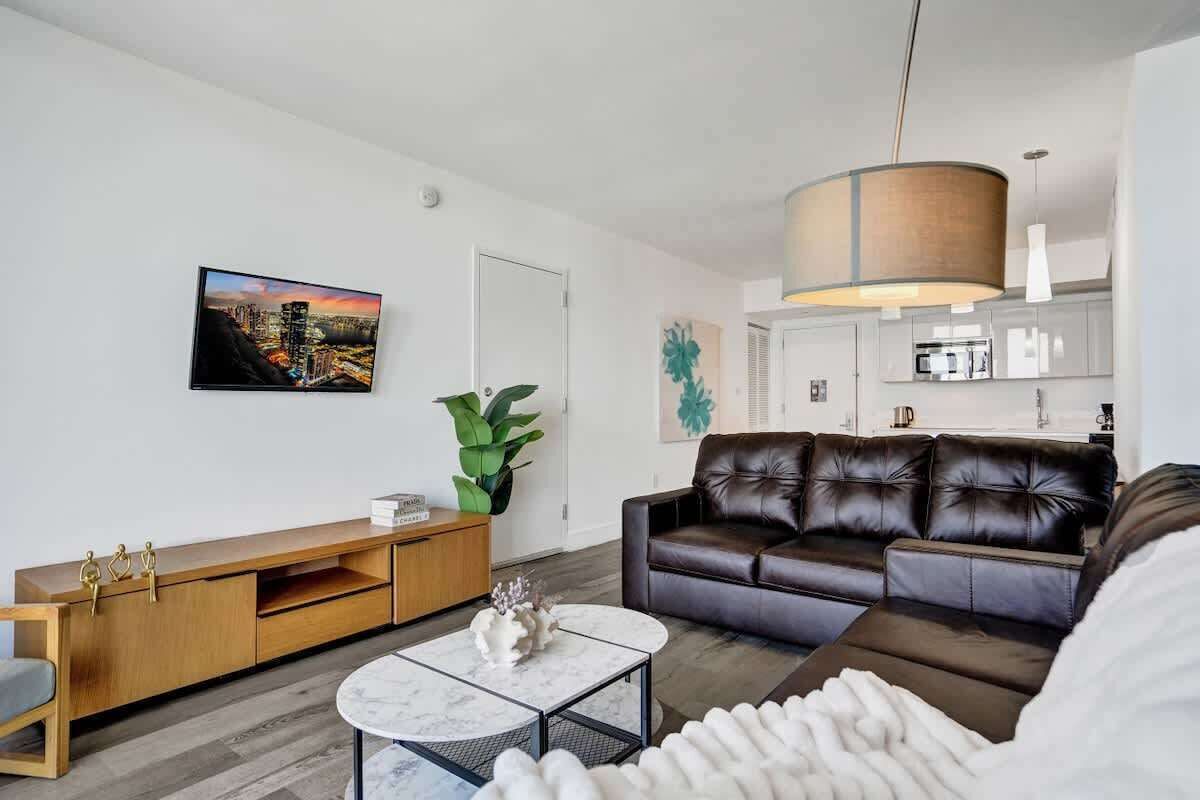 Ein modernes Wohnzimmer mit einer Ledersofa, einem Holz-TV-Möbel, einem Marmor-Couchtisch und einer großen Pflanze.