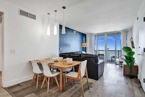 Un salon moderne comprenant un coin repas, un canapé en cuir noir et une grande fenêtre donnant sur la ville.