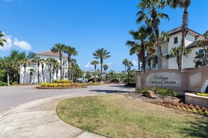 Een woongebied met een bord waarop 'Villages Crystal Beach' staat, palmbomen en huizen met rode dakpannen.