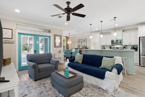 A modern living room with a sofa, ottoman, and a dining area with chairs. - Tahitian Treasure - Villages of Crystal Beach (Destin)