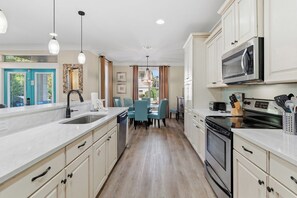 A kitchen with a sink, stove, microwave, and dining area with chairs. - Tahitian Treasure - Villages of Crystal Beach (Destin)
