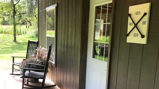 A wooden porch with a rocking chair, a doormat, and a wall-mounted compass sign.