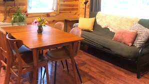 A wooden interior with a dining table, chairs, a sofa, and a television.