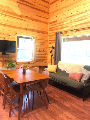 A wooden interior with a dining table, chairs, a sofa, and a television.