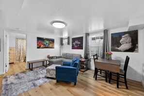 A modern living room with a sectional sofa, a dining table, and a large window. - Lander & Mt Rose Duo | Near Midtown & Downtown (Reno)