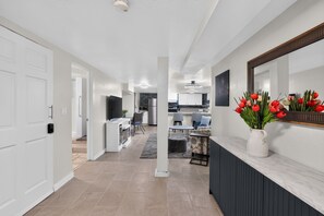 Een moderne keuken met een flatscreen televisie, een eethoek met een tafel en stoelen, en een gang die leidt naar een deur.