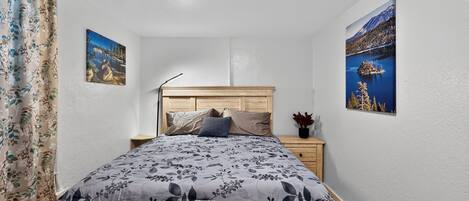 A bedroom with a bed, nightstand, and two wall-mounted pictures.