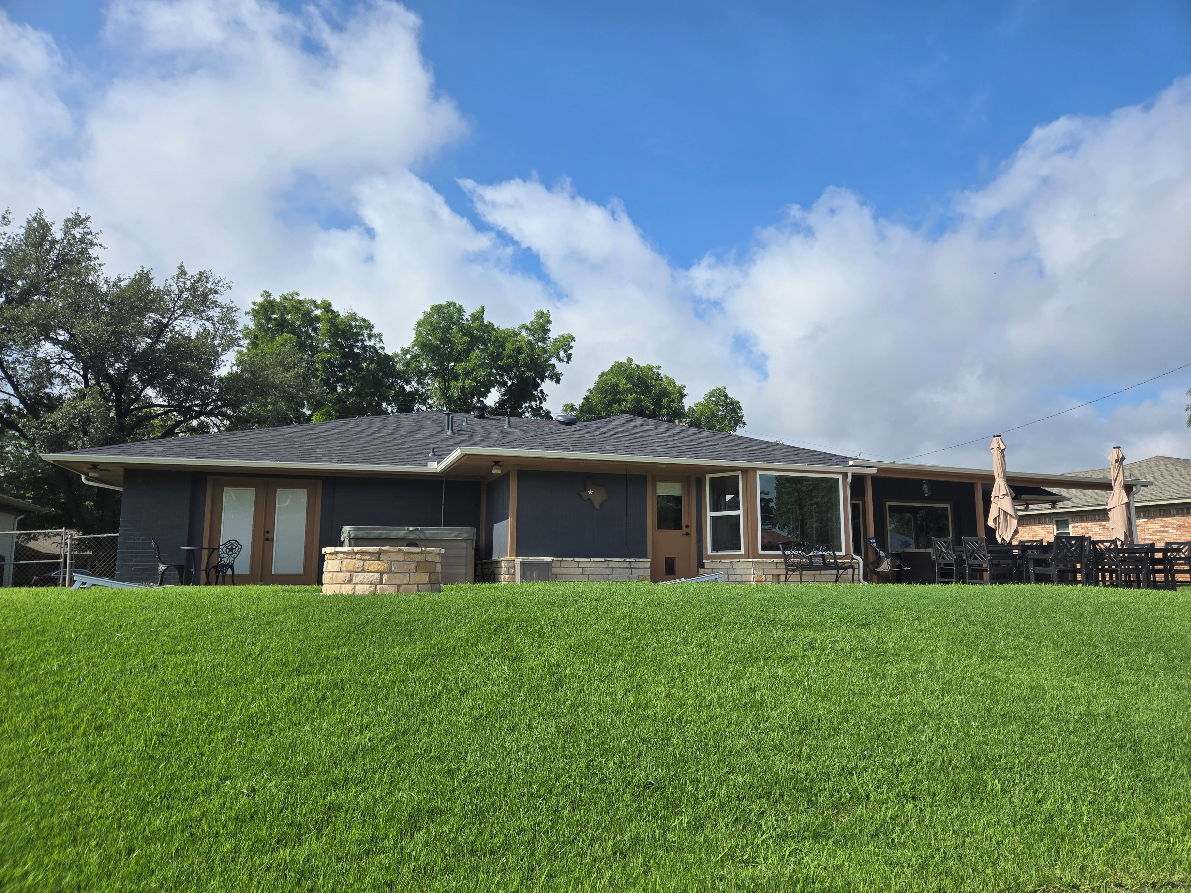 A residential house with a covered patio, a stone fireplace, and a well-maintained lawn.