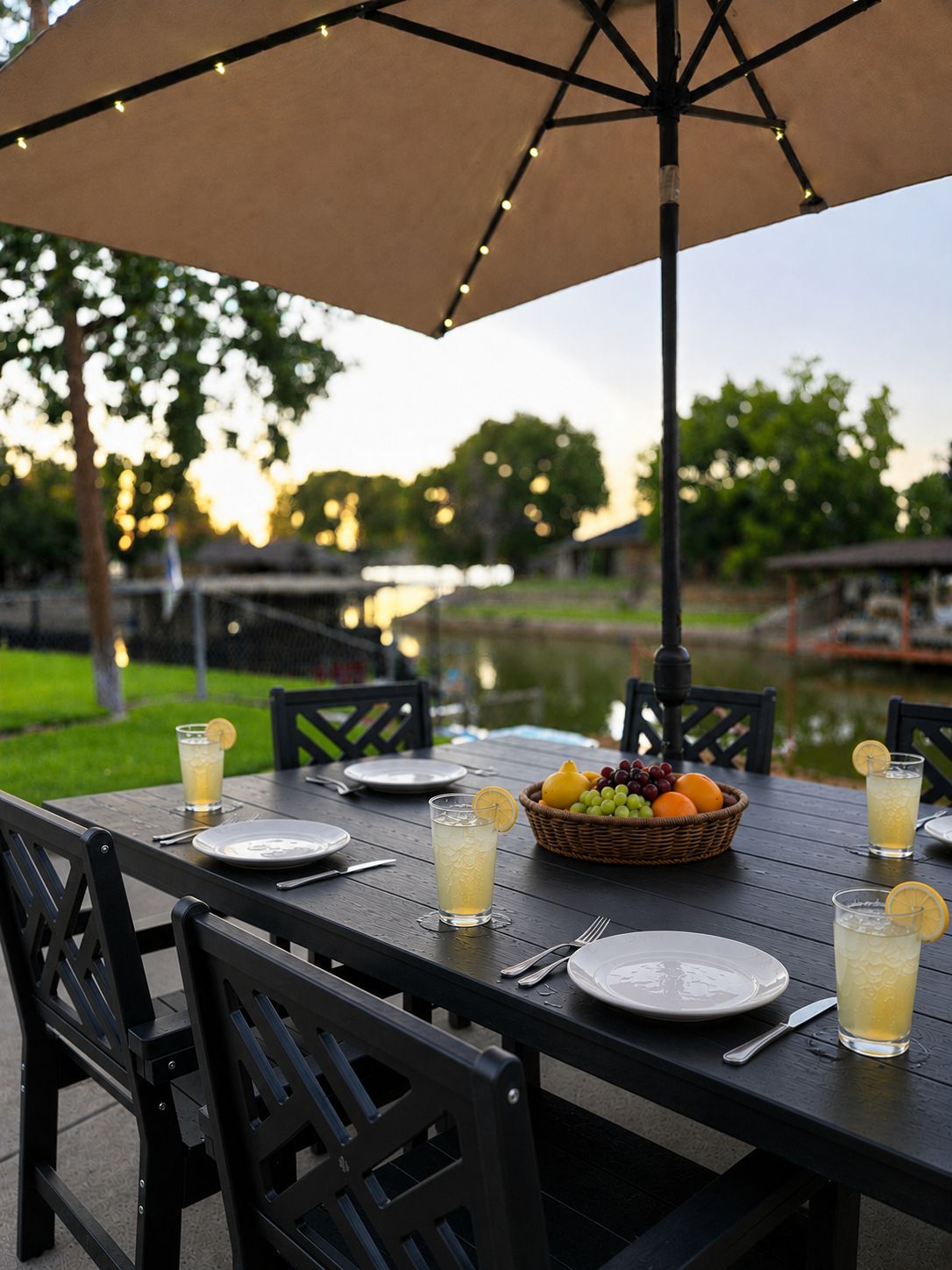 An outdoor dining area with a table set for two, a basket of fruit, and drinks.