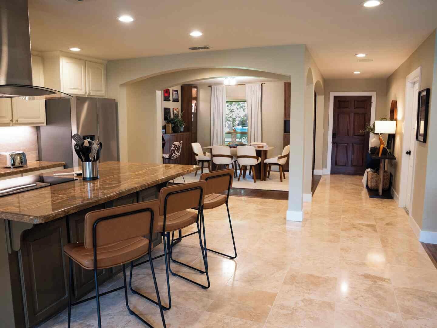 A modern kitchen with a central island, bar stools, and a dining area with a table and chairs.
