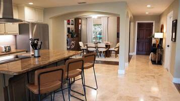 A modern kitchen with a central island, bar stools, and a dining area with a table and chairs.