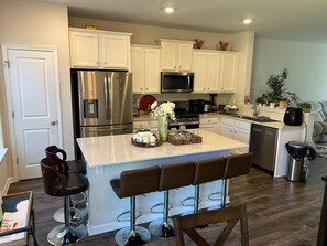 A modern kitchen with white cabinets, stainless steel appliances, a central island with bar stools, and a dining area with a sofa. - Beautiful Townhouse 4 bedroom 3  bathroom in Fogelsville PA (Fogelsville)