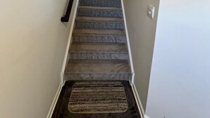 A carpeted staircase with a handrail, a doormat at the bottom, and a light switch on the wall. - Beautiful Townhouse 4 bedroom 3  bathroom in Fogelsville PA (Fogelsville)