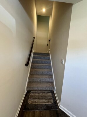 A carpeted staircase with a handrail, a doormat at the bottom, and a light switch on the wall. - Beautiful Townhouse 4 bedroom 3  bathroom in Fogelsville PA (Fogelsville)