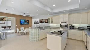Uma cozinha moderna com eletrodomésticos embutidos, um espaço de refeições com mesa de vidro e uma TV fixada na parede.