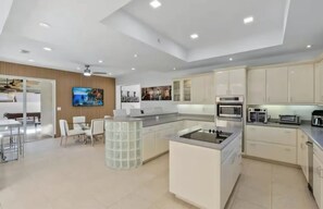 A modern kitchen with built-in appliances, a dining area with a glass-top table, and a TV mounted on the wall. - Villa Caleta (Miami)