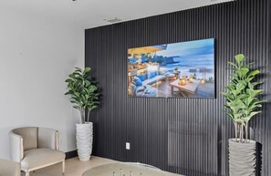 A modern living room with a large TV mounted on a dark wall, two potted plants, a beige sofa, and a wooden coffee table. - Villa Caleta (Miami)