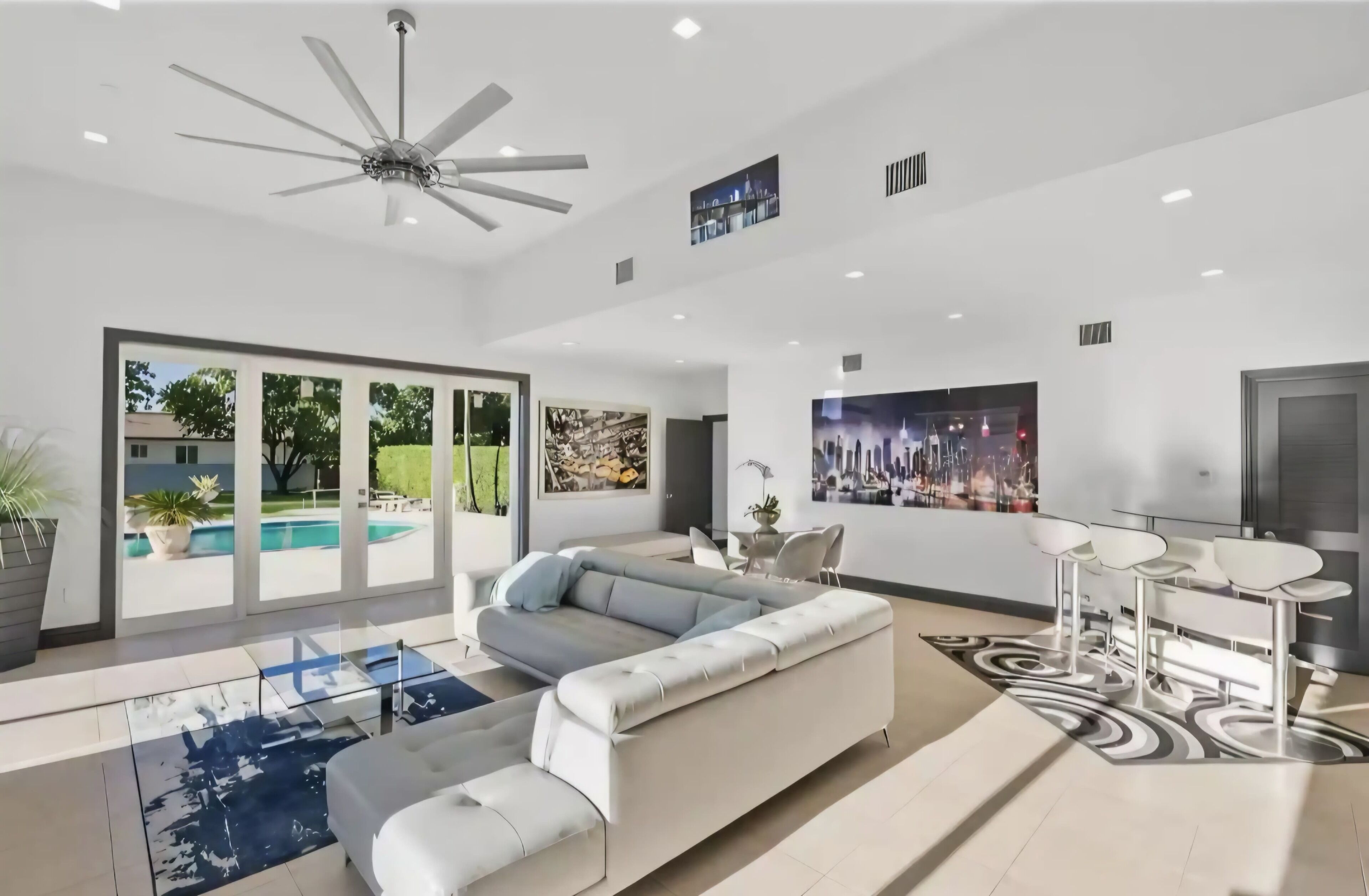 A spacious living area with a large sofa, a dining table with chairs, and a ceiling fan.