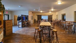 Un vaste espace dédié à la salle à manger, avec une longue table en bois et de nombreuses chaises, un coin bar avec des tabourets, et une vue dégagée grâce à de grandes fenêtres.