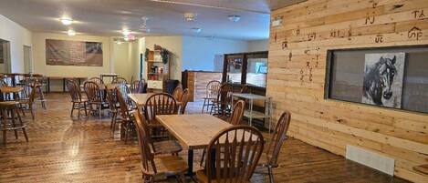 A restaurant with wooden floors, tables, and chairs. There is a large framed picture on the wall and a menu board.