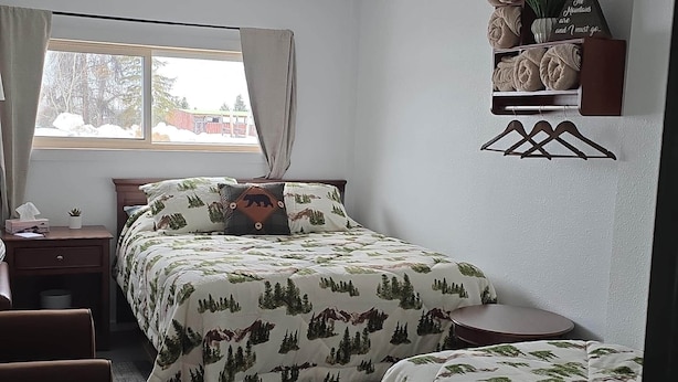 Une chambre avec deux lits, une fenêtre, une table de chevet, une chaise et une étagère murale où sont rangées des serviettes.