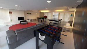 Ett modernt vardagsrum med ett fotbollsspel, ett biljardbord och en platt-TV.